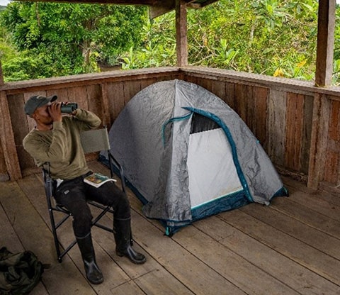 Man looking through binoculars sitting near a tent Bai Camping in Odzala-Kokoua National Park